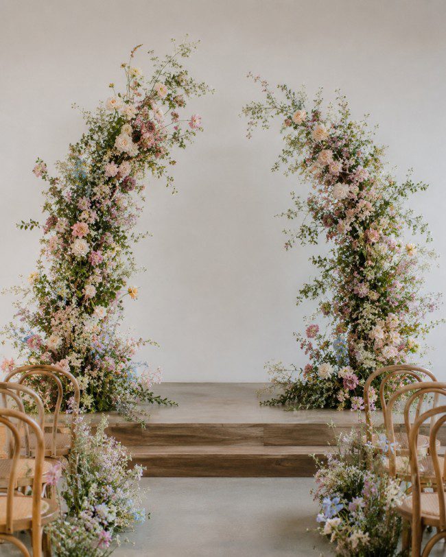 Modern broken-style floral wedding arch with asymmetrical white and green seasonal flowers, creating an elegant ceremony backdrop in Melbourne.